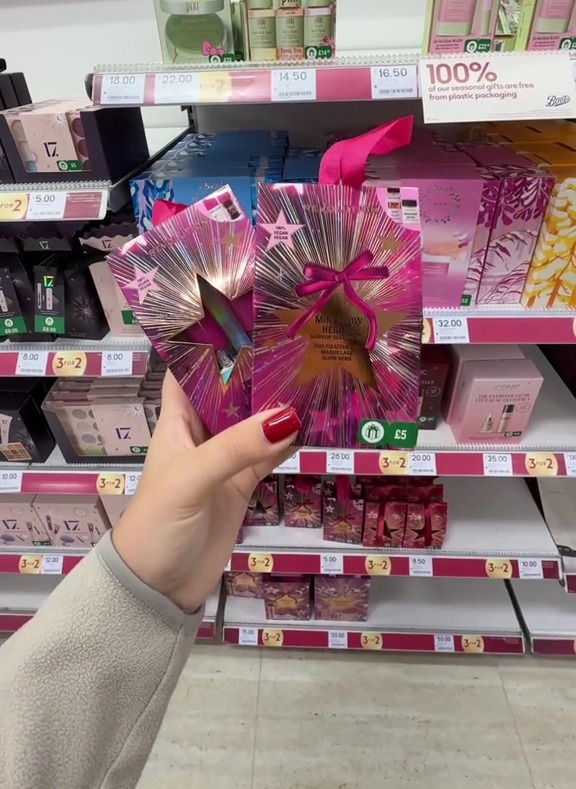 A hand holding a pink and gold "Mini Glow Heroes" makeup gift set in a store.