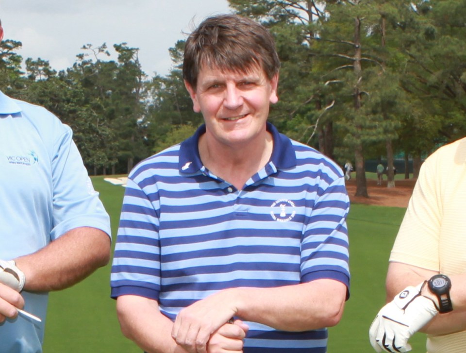 Four men standing on a golf course with clubs, in front of a Masters scoreboard.