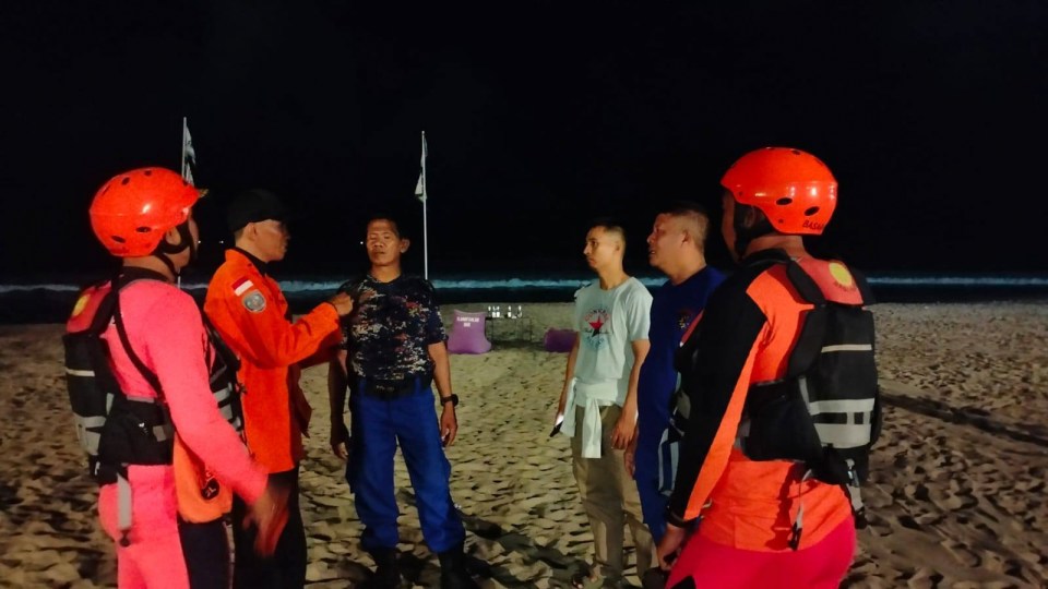 Rescue teams and friends on a beach at night searching for a missing British tourist in Bali.