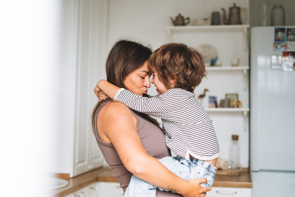 Pregnant woman holding and hugging her son in a kitchen.