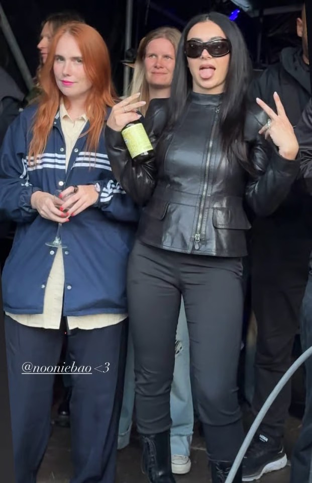 Charli XCX in a black leather outfit with a friend in a navy jacket.