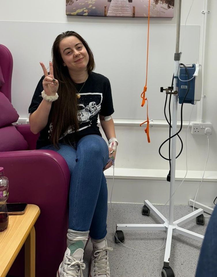 Lauren Ayres in the hospital with an IV drip in her arm, making a peace sign with her fingers.