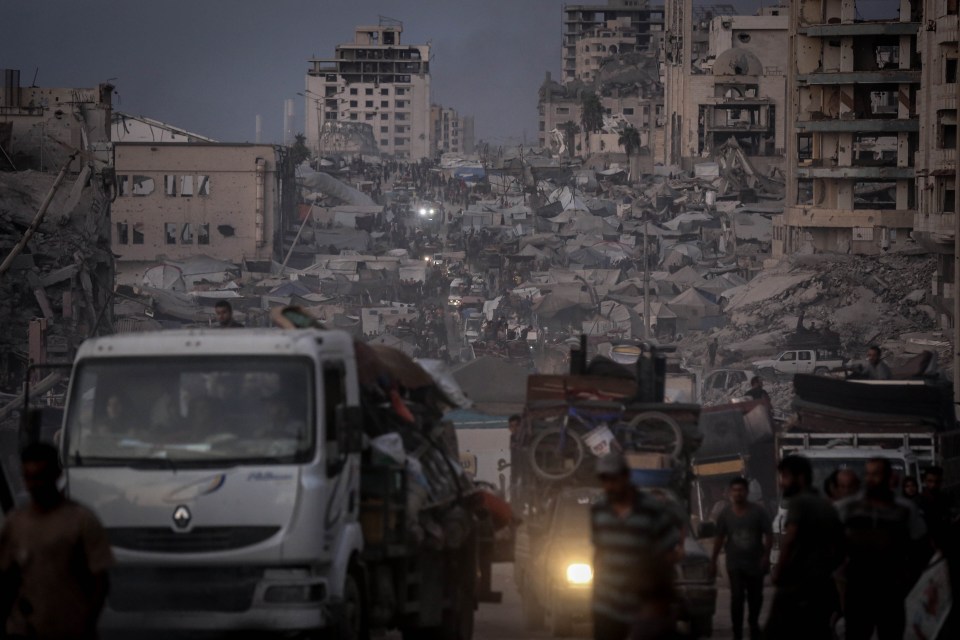 Palestinians, including children, in Gaza City center migrate towards southern regions with belongings amidst destroyed buildings and a makeshift tent city.