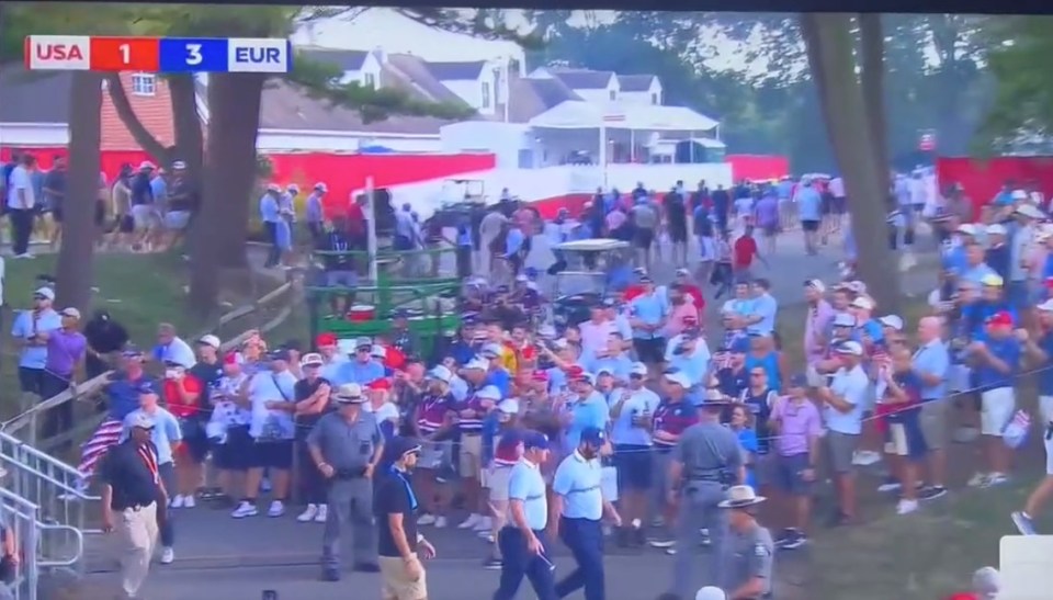 A golf score update on a TV screen shows USA with 1 point and EUR with 3 points, with a crowd of spectators in the background.