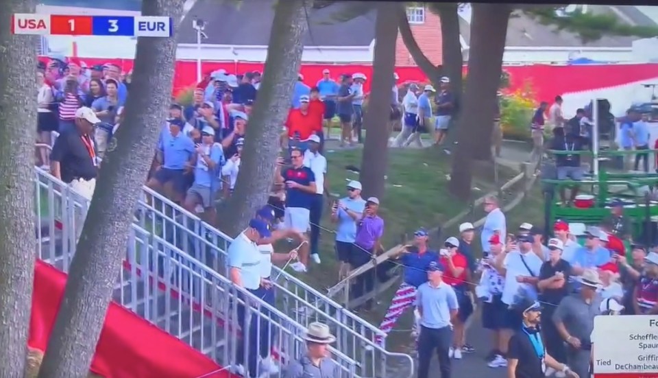 A crowd of spectators at a golf tournament, with a scoreboard in the top left showing USA 1 EUR 3.
