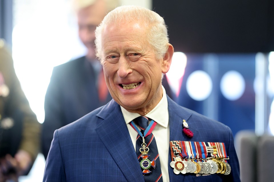 King Charles III smiling and wearing medals on his suit.