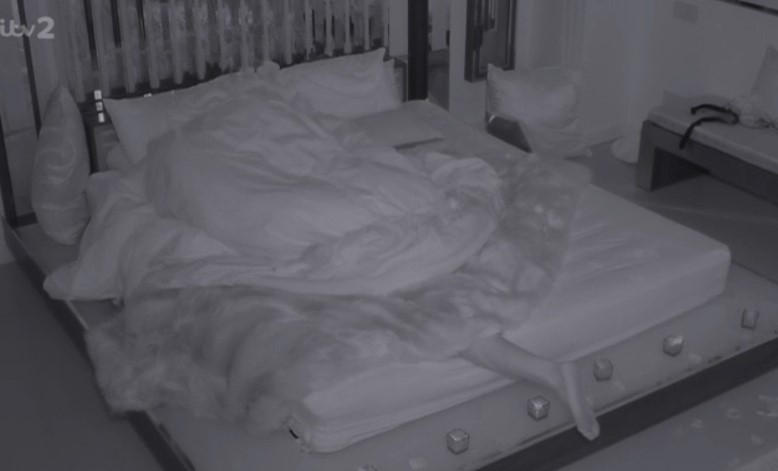 A low-light image of a bed with a person's foot sticking out from under the covers.