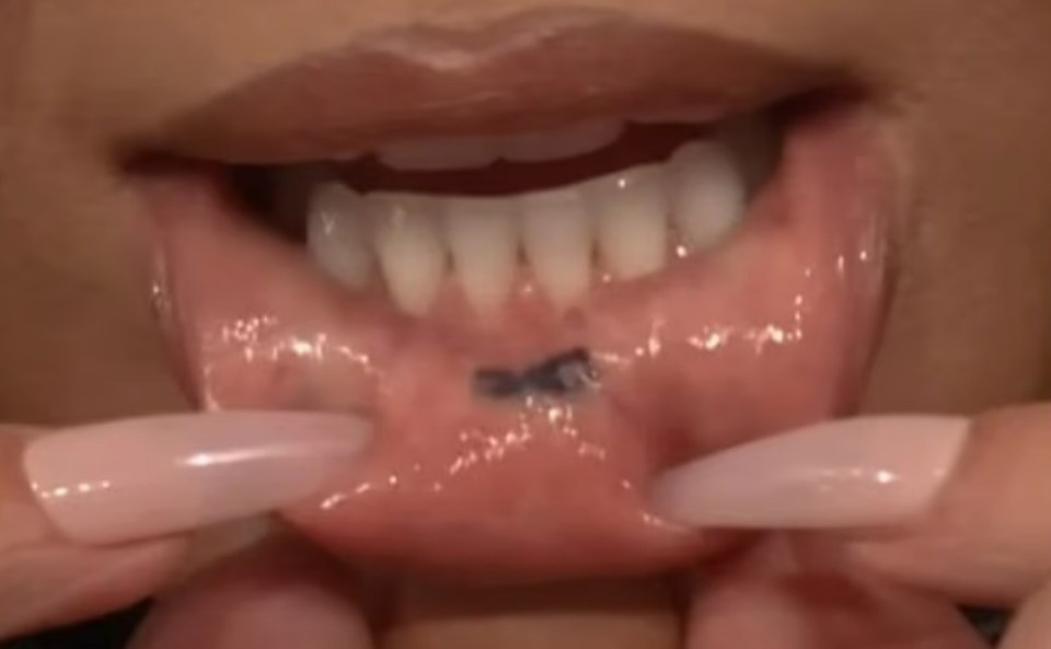 Close-up of a person revealing an infinity symbol tattoo on the inside of their lower lip.