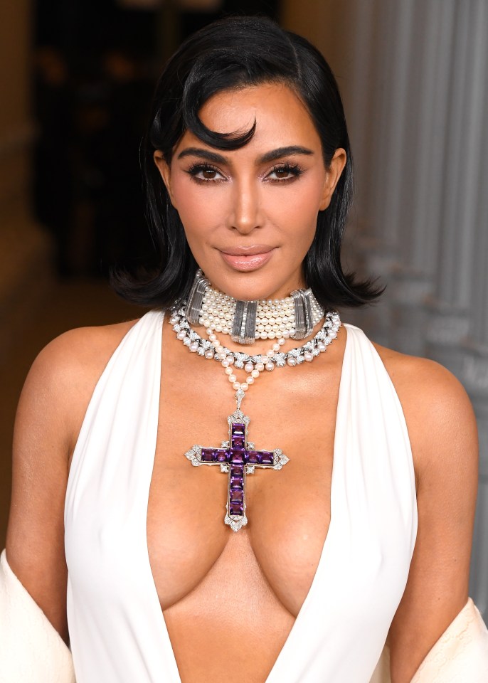 Kim Kardashian wearing a white plunging halter top and an oversized layered pearl and diamond choker with a large amethyst cross pendant.