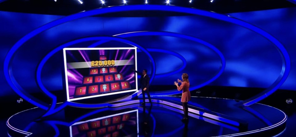 Two people on a game show stage, one pointing to a screen with "£25,000" and a grid of numbered panels.