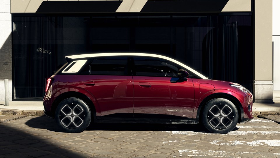 Red Aion electric car parked on cobblestones.