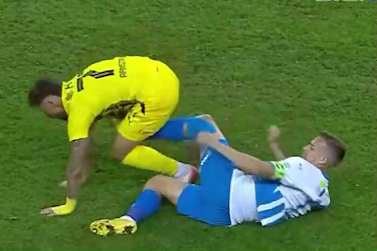 Nicusor Bancu in a yellow jersey falling near a player in a blue and white jersey on a green grass field.