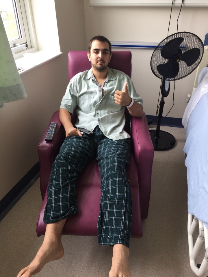 Nick Barnard, a man with a medical bracelet, gives a thumbs up while sitting in a hospital room.