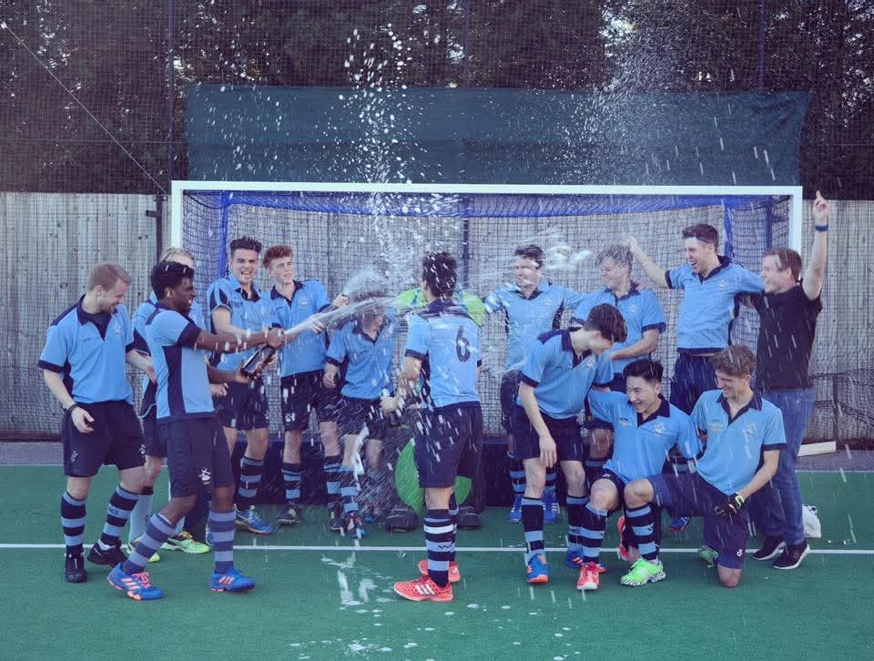Nick Barnard celebrating with his hockey team, spraying a bottle of champagne in front of a goal net.