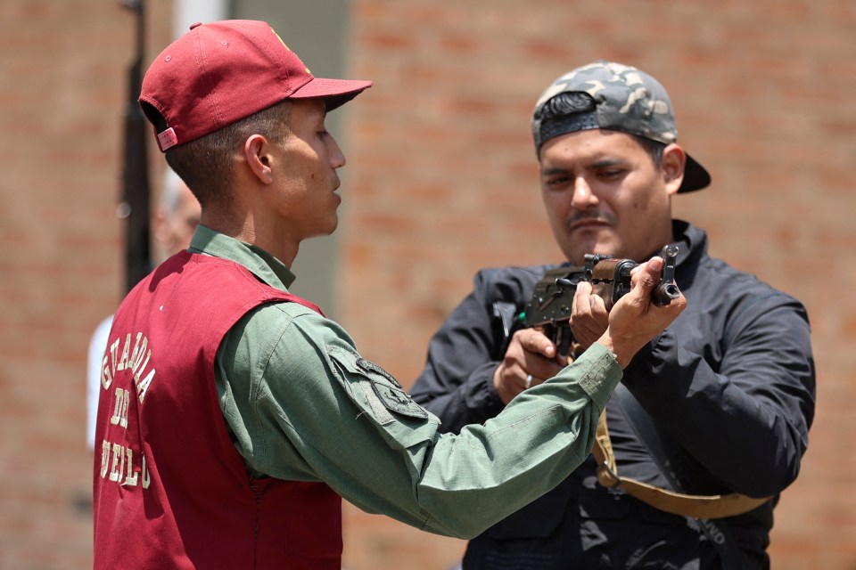 A man in a red vest and red cap giving instructions on holding a rifle to another man in a black jacket and camouflage cap.