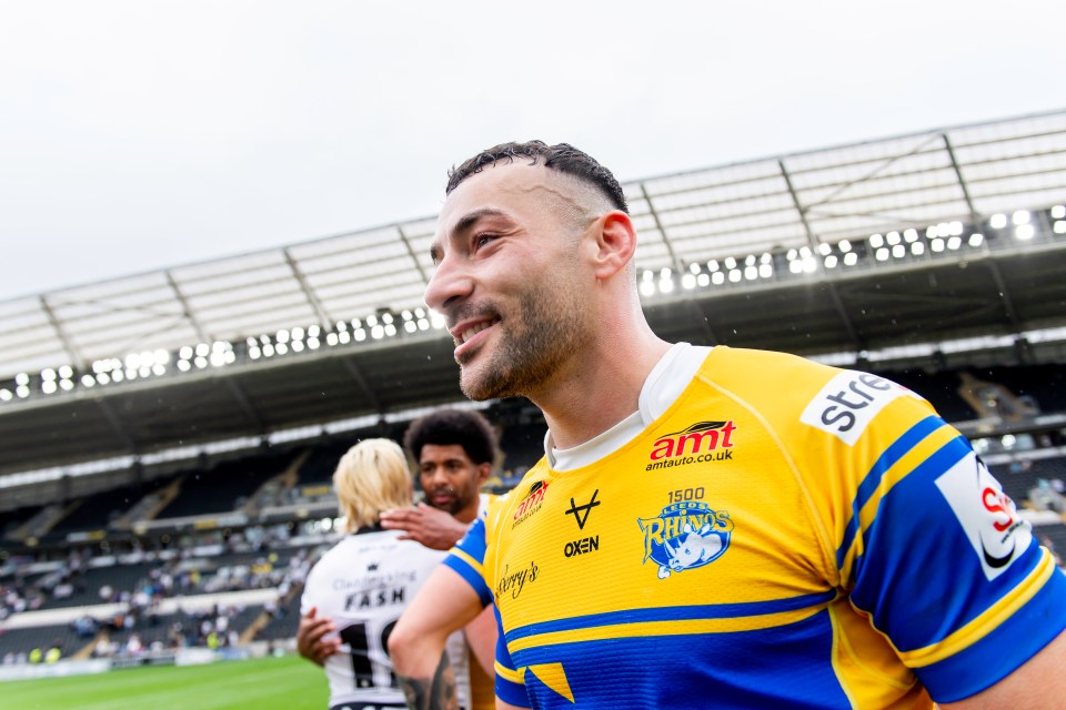 A man in a yellow and blue jersey with the Leeds Rhinos logo smiles after a rugby match.