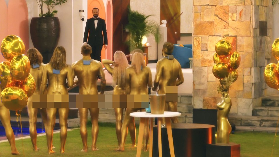 Rylan Clark-Neal in a tuxedo with a group of people painted gold, at a Goldfinger-themed party.