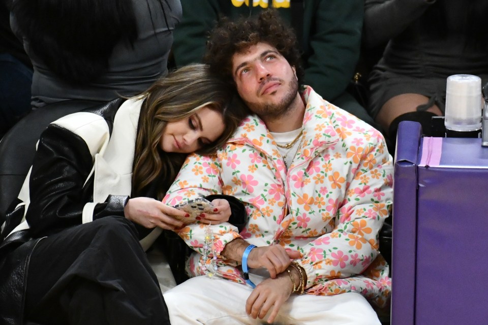 Selena Gomez leans her head on Benny Blanco's shoulder while holding her phone at a basketball game.