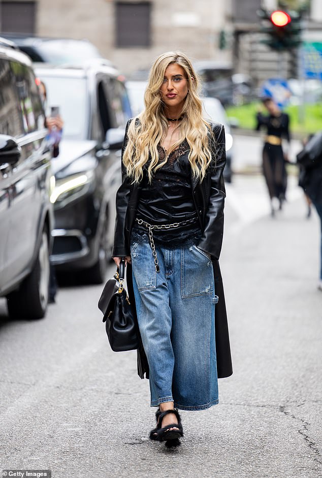 Emili Sindlev cut a casual display in a pair of light blue denim jeans, a satin vest and a black leather trench coat