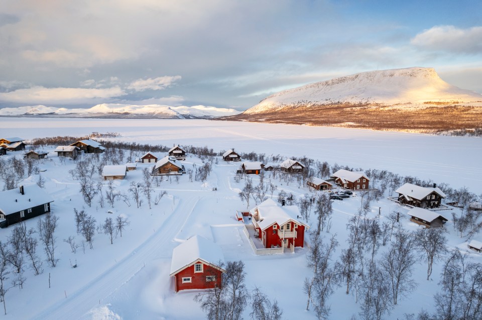 Aerial view of an arctic sunset over a traditional mountain village by a frozen lake in Kilpisjarvi, Enontekio, Lapland, Finland.