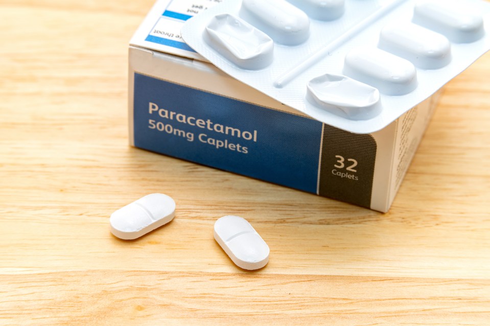 A generic box of Paracetamol 500mg Caplets and two pills on a wooden surface.
