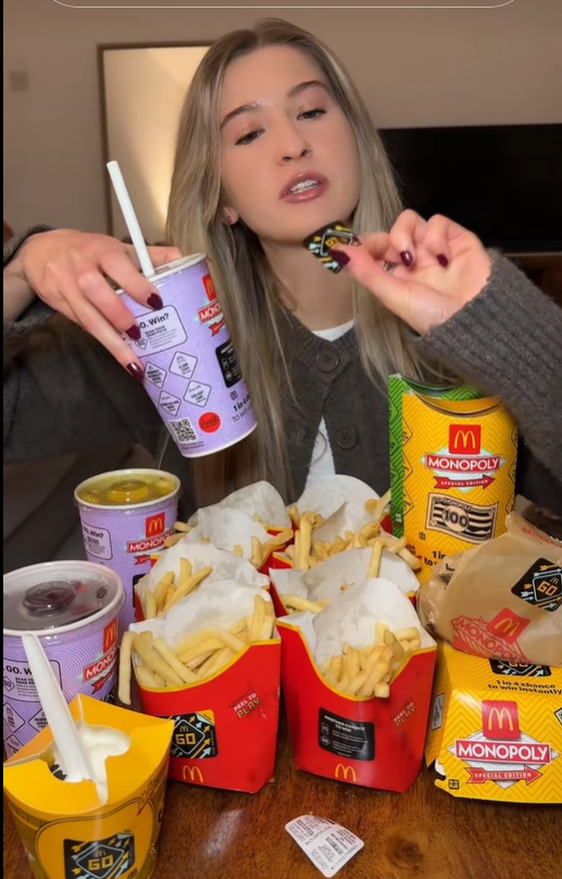 A woman holding a McDonald's Monopoly game piece surrounded by many McDonald's food items.