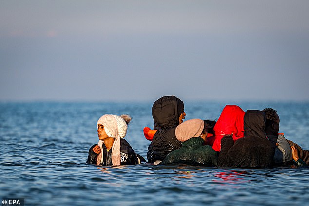 Migrants wade through water to board an inflatable boat during an attempt to cross the English Channel