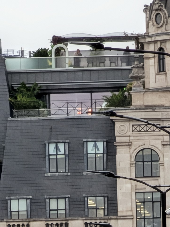 Roofs of buildings with a person on an outdoor patio and streetlights in the foreground.