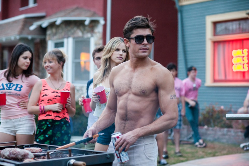 Zac Efron shirtless with a muscular physique, smiling at the camera.
