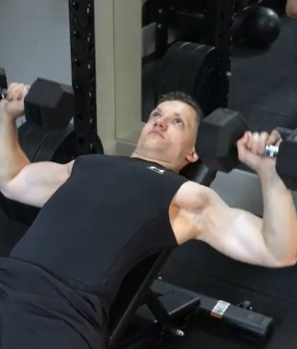 Man doing a dumbbell incline press in a gym.