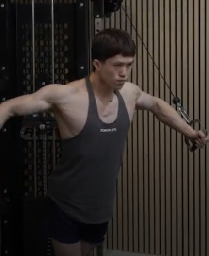 Man in a gray tank top working out on a cable machine.