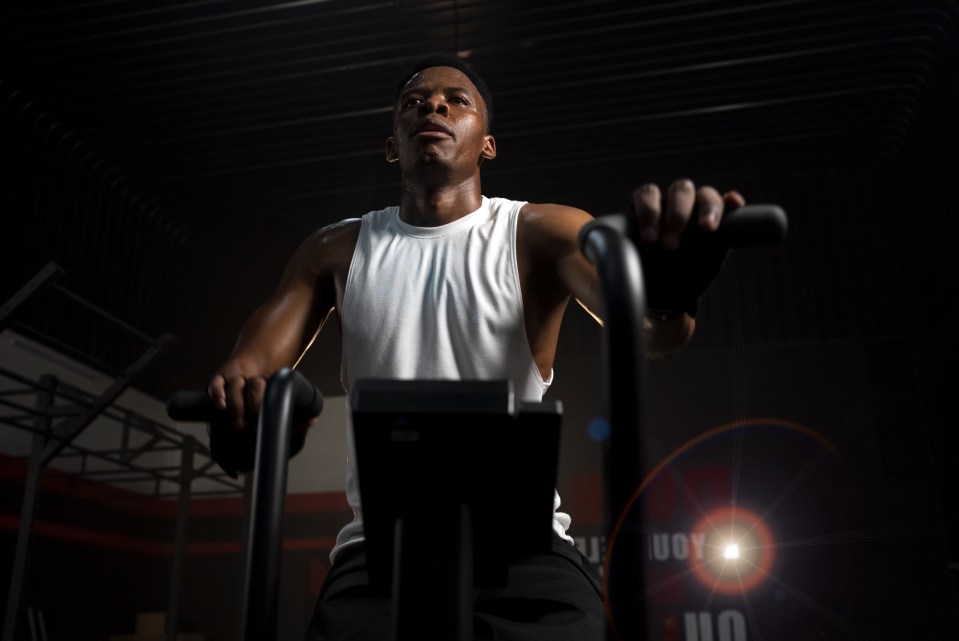 Sweaty man in white tank top doing cardio on an exercise machine.