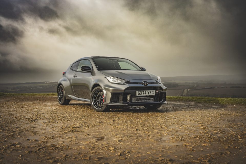 Silver Toyota GR Yaris parked on a muddy path under a cloudy sky.