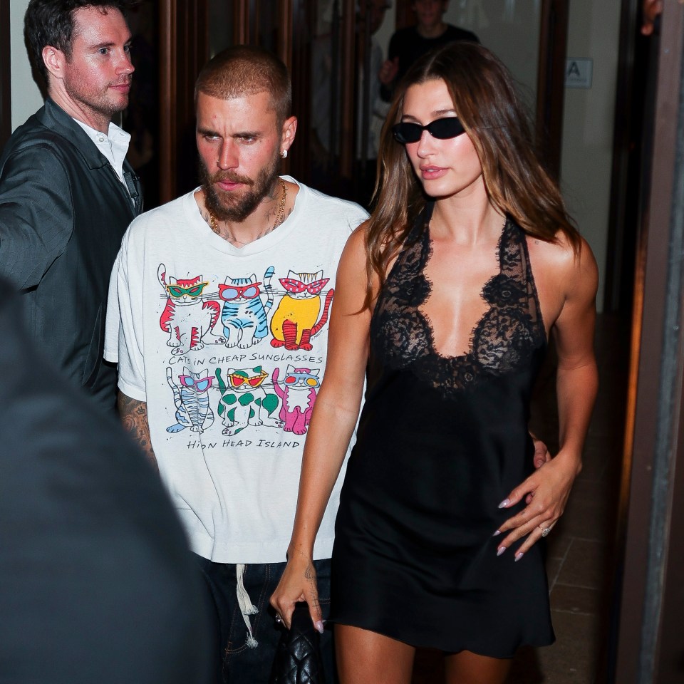 Justin Bieber in a white t-shirt with a graphic cat design and Hailey Bieber in a black lace and satin mini-dress and sunglasses.