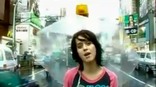 A young woman with dark hair and a pink and black shirt in a city street.