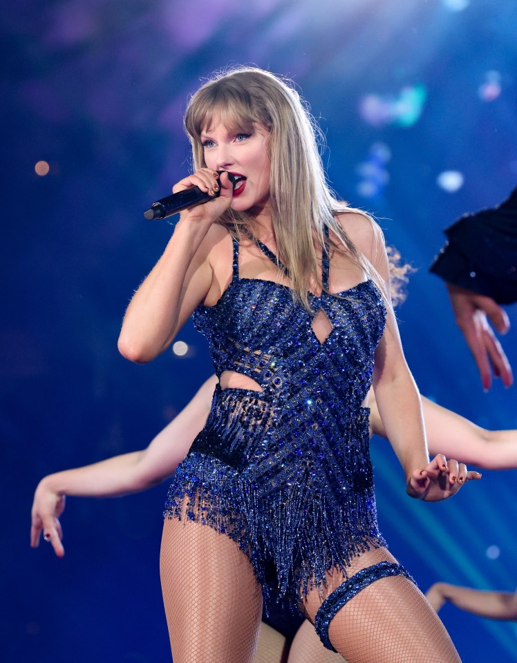 Taylor Swift performing on stage in a sparkly blue outfit and holding a microphone.