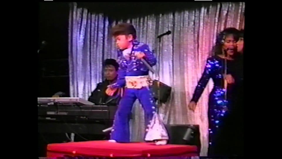 Bruno Mars performing as a child on stage in an Elvis-like blue jumpsuit.