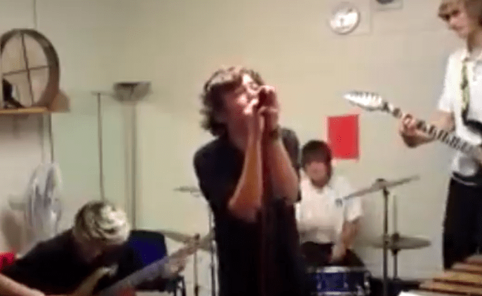 A band with a singer holding a harmonica and guitarists in a room.