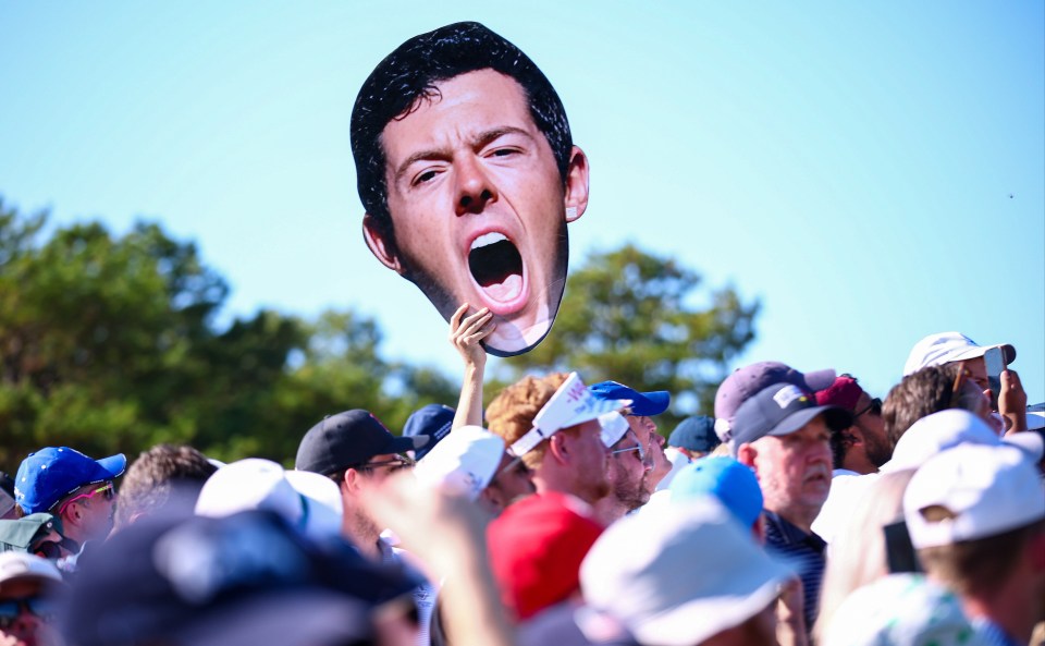 A supporter holding a sign of Rory McIlroy's face with his mouth open in an excited expression above a crowd.