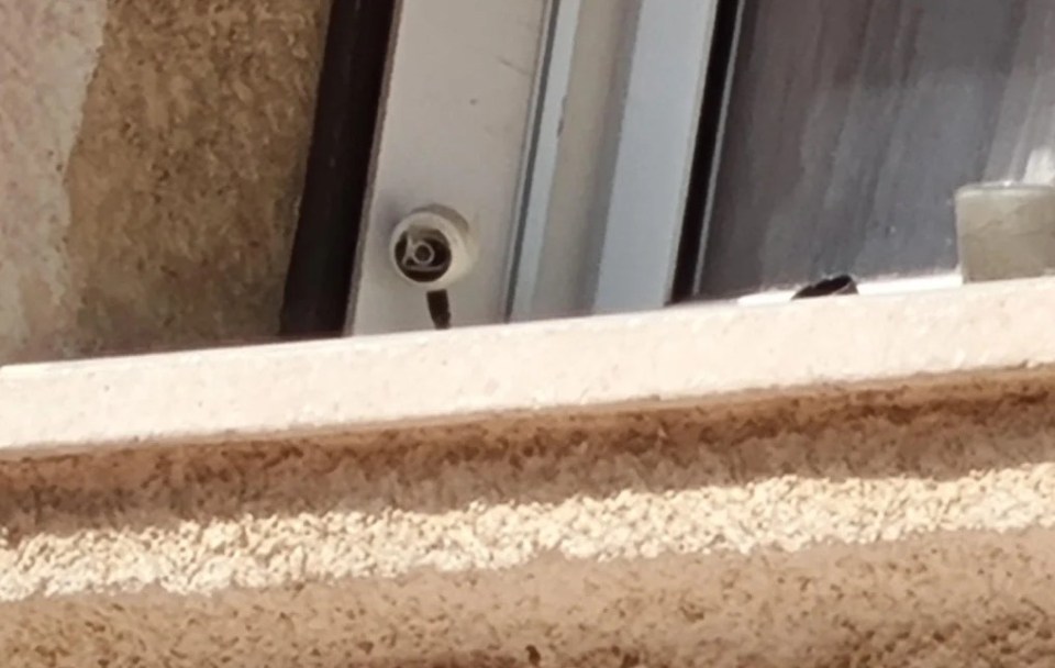 A security camera mounted on a window frame, pointing outwards.