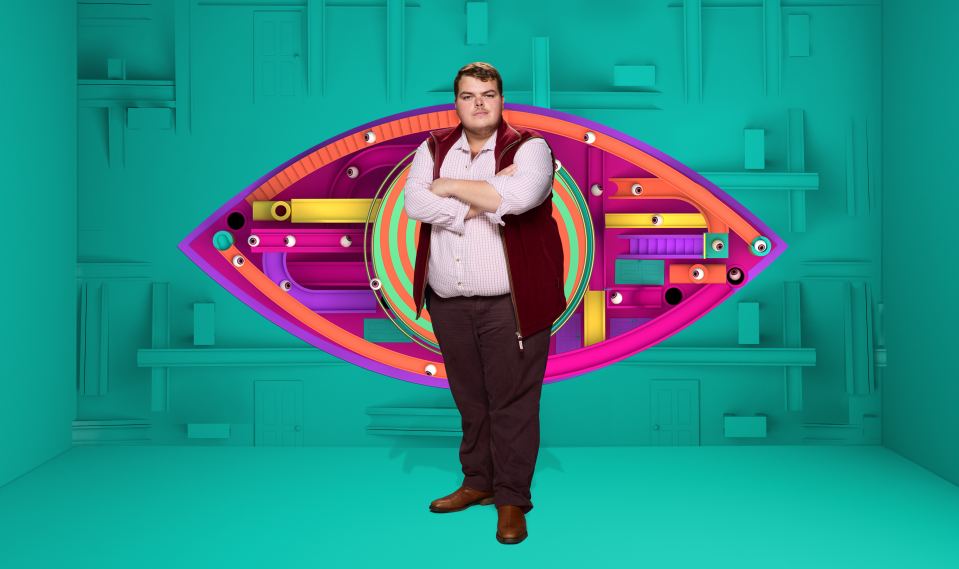 Big Brother contestant Cameron K. standing with his arms crossed in front of a colorful Big Brother eye logo.