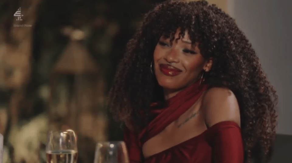 A woman with curly hair smiles while wearing a red dress.