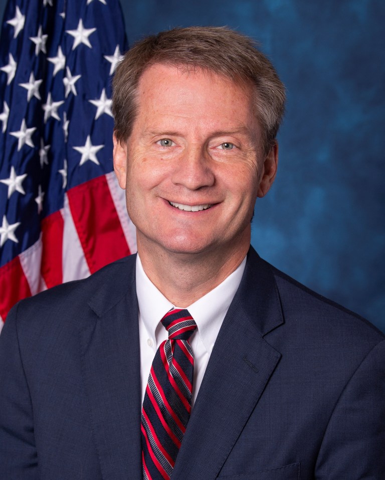 U.S. Rep. Tim Burchett smiling in front of an American flag.