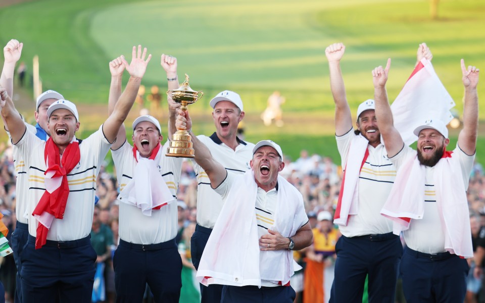 Rory McIlroy lifts the Ryder Cup trophy surrounded by celebrating Team Europe golfers.