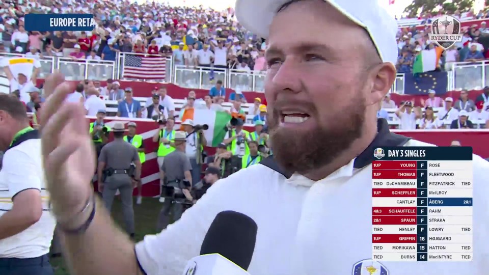 Shane Lowry, with a beard and white cap, appears emotional during a Ryder Cup event, with a scoreboard displaying "DAY 3 SINGLES" and game results.