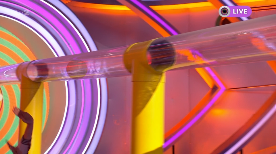 Someone's body in a clear plastic tube on a colorful game show set.