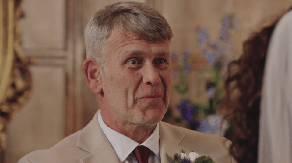 A man in a light suit and red tie looking at something with wide eyes and a slight smile.