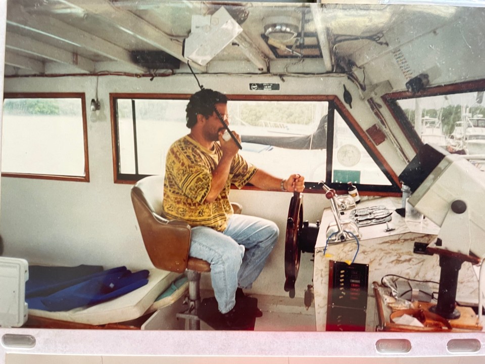Martin Suarez at the helm of a boat, speaking into a radio.