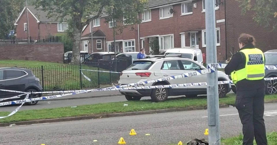 Police scene with a car and police tape in the foreground, and residential buildings in the background.