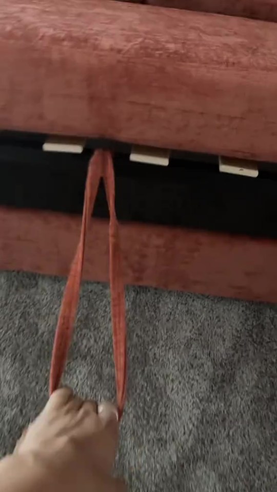 A person pulling an orange fabric strap to open a sofa bed.